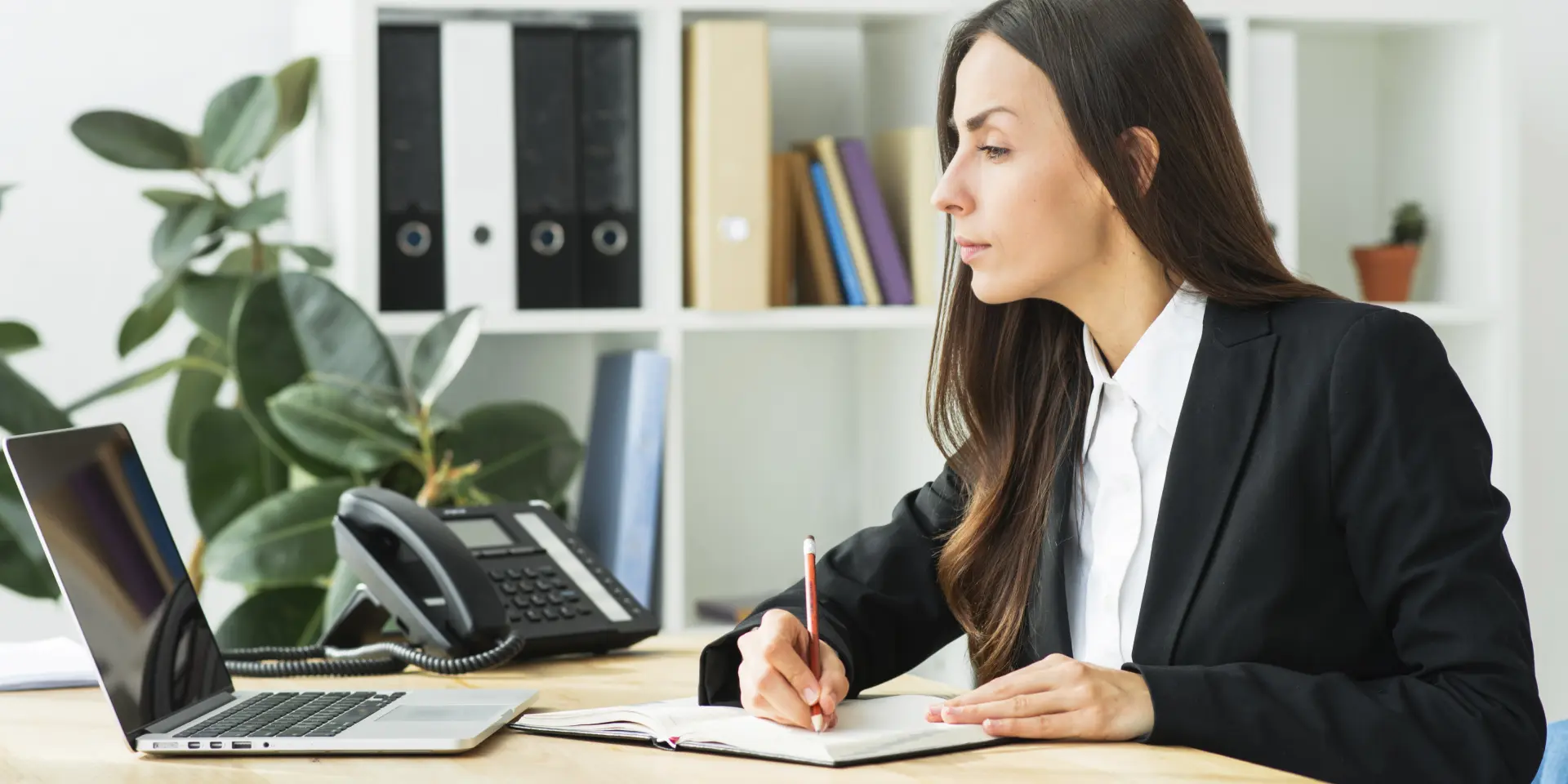 Fotografía de una mujer en una oficina trabajando con un ordenador portátil y tomando anotaciones