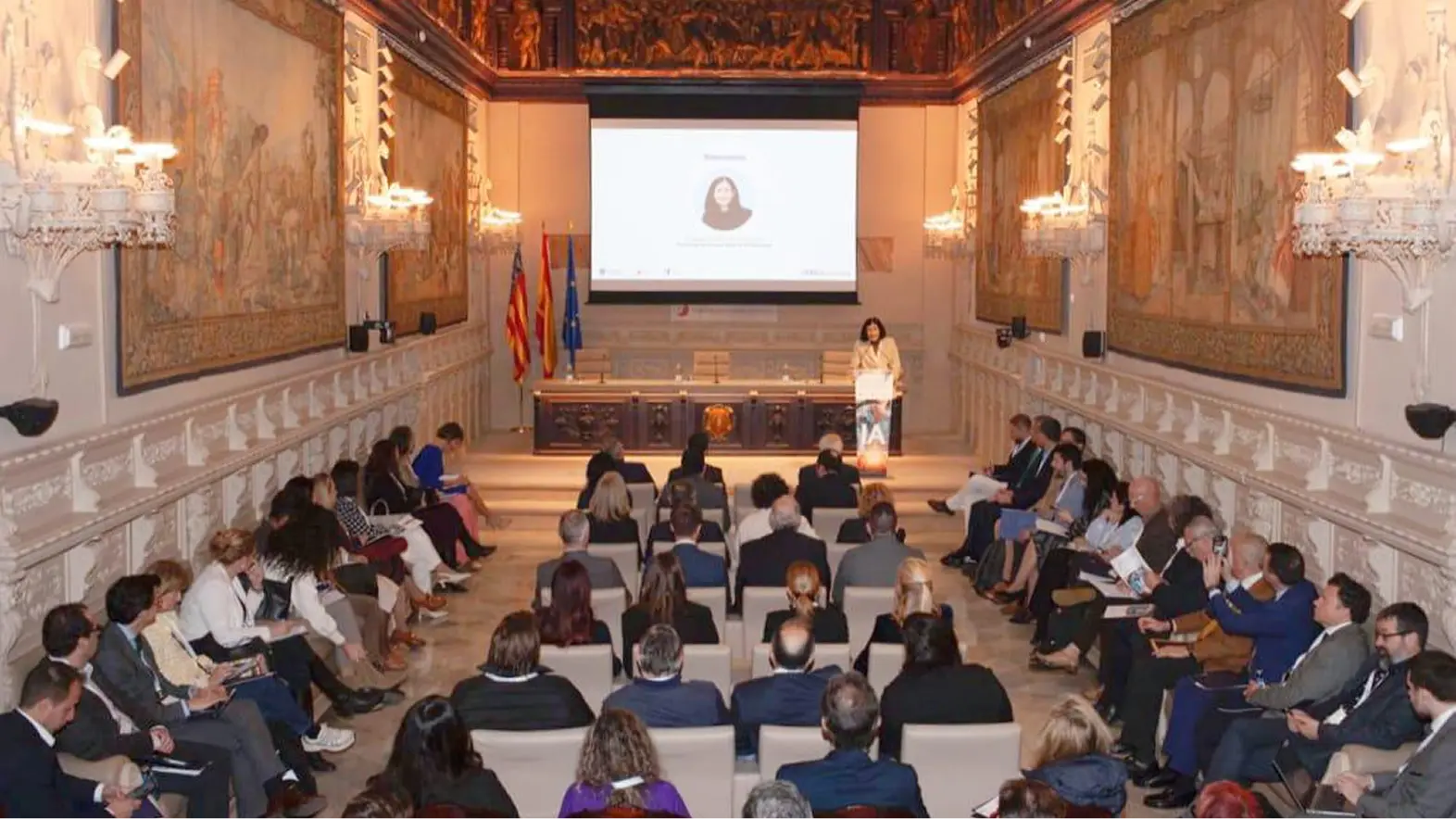 Fotografía con una sala repleta por el público mientras la Presidenta del Consejo General del Notariado, Concepción Pilar Barrio Del Olmo, habla en el escenario al fondo