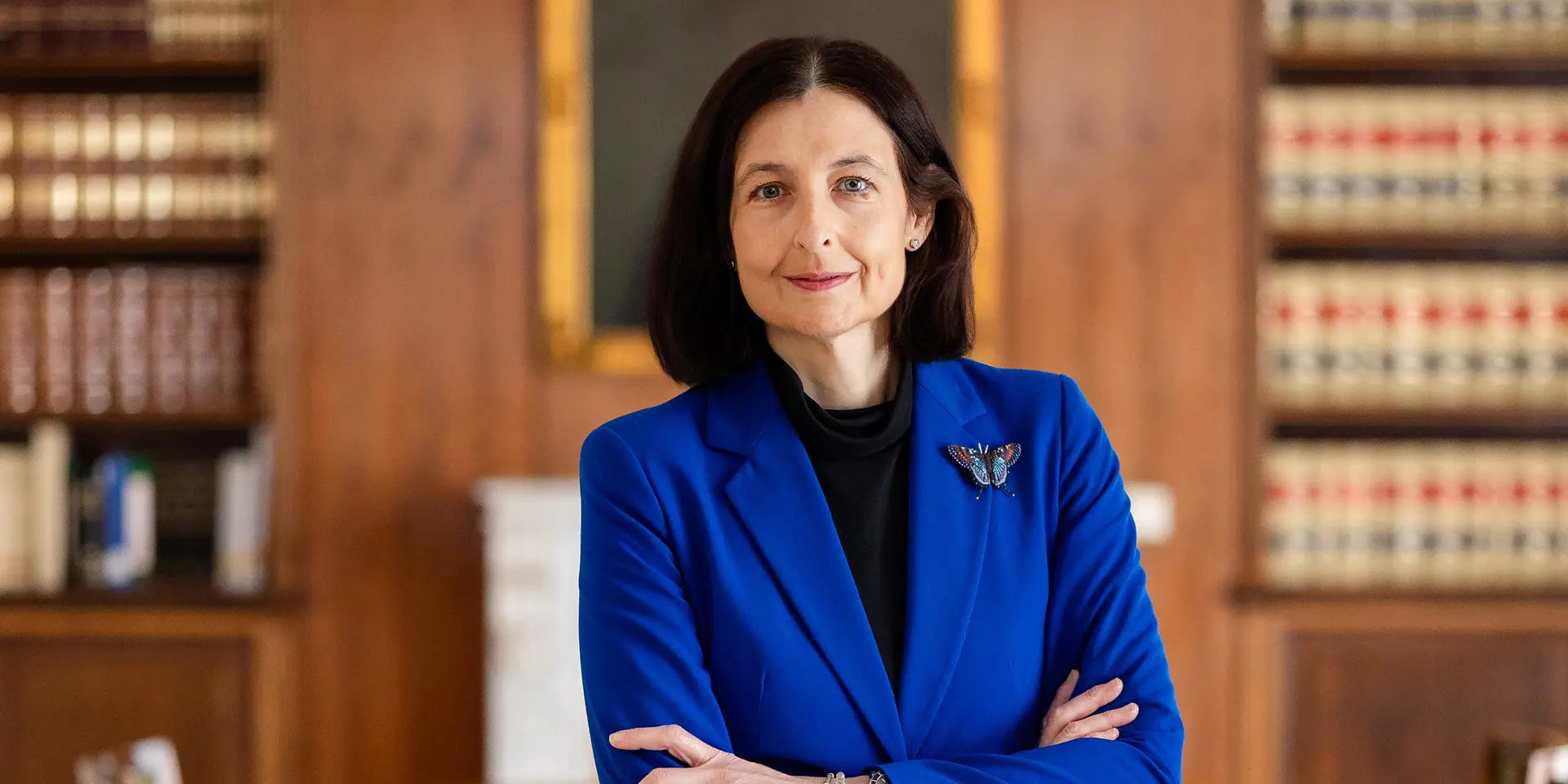 La presidenta del Notariado de pie en una biblioteca con los brazos cruzados.